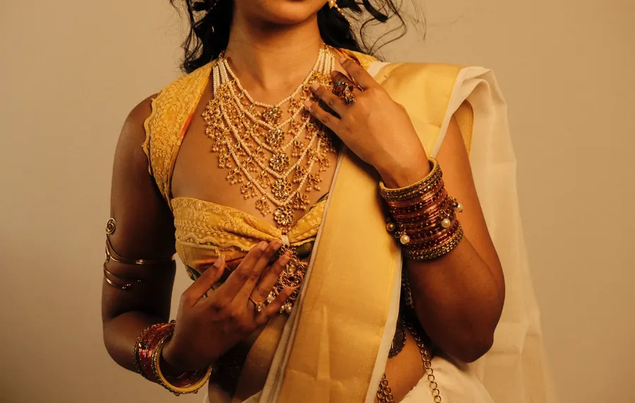 Detail of layered gold jewellery and bangles over a cream sari