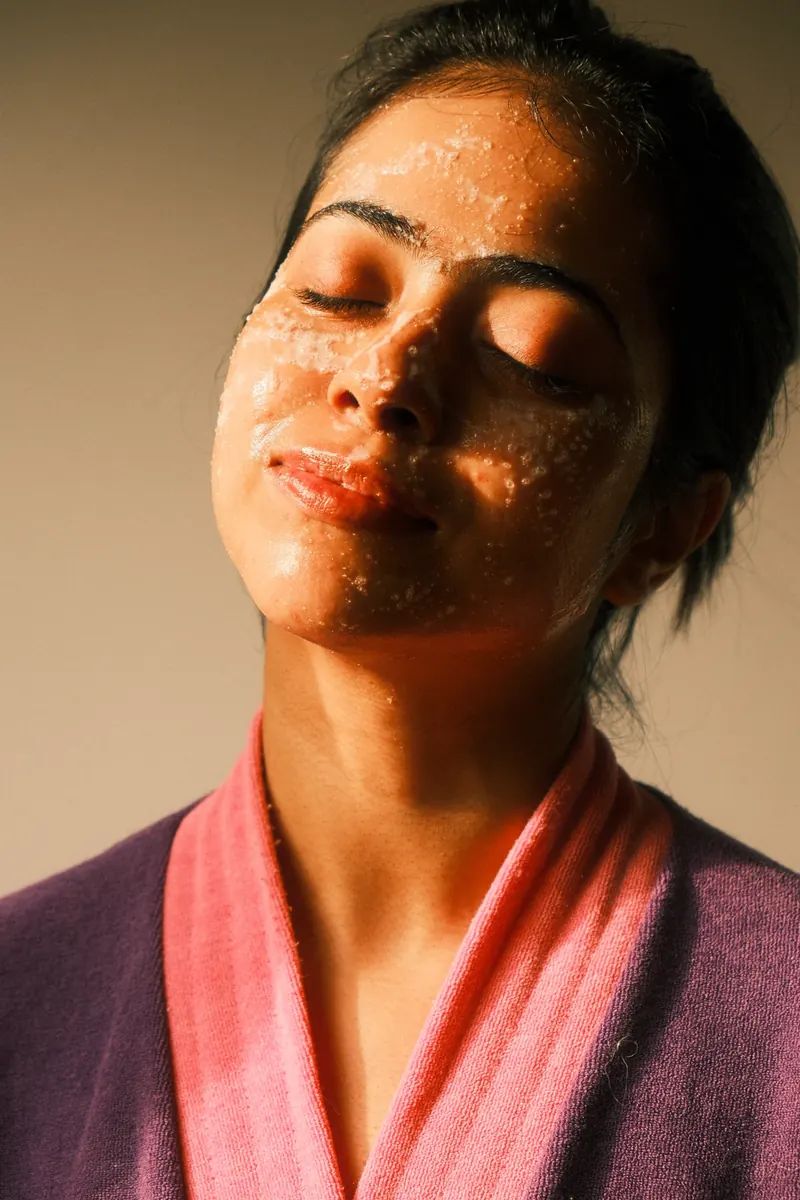 Sandipta in slatted sunlight with a skincare scrub on her face